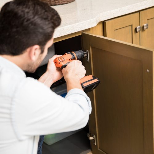 Point of view of a young handyman using a power drill to fix a door in a kitchen cabinet